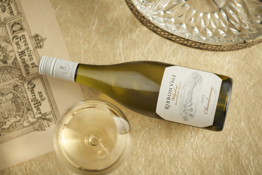 A bottle of Ribbon Vale 2022 chardonnay laying on a table with a full glass of wine